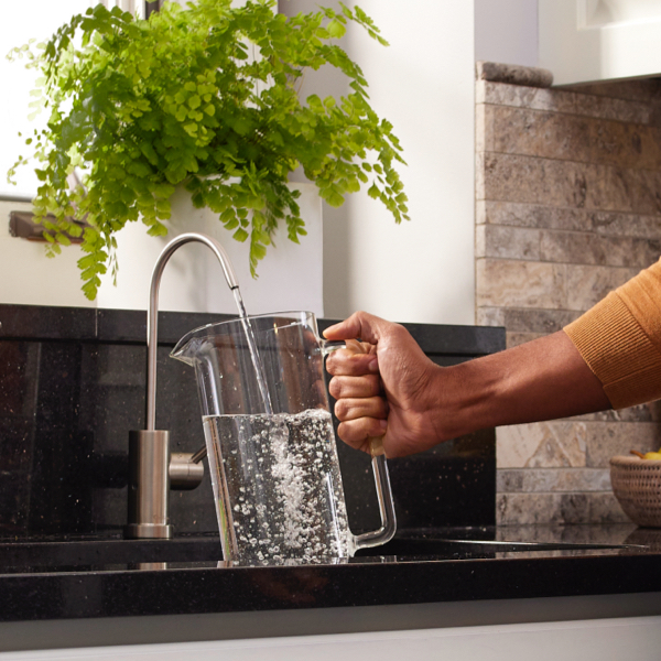 person collecting water into a glass kettle